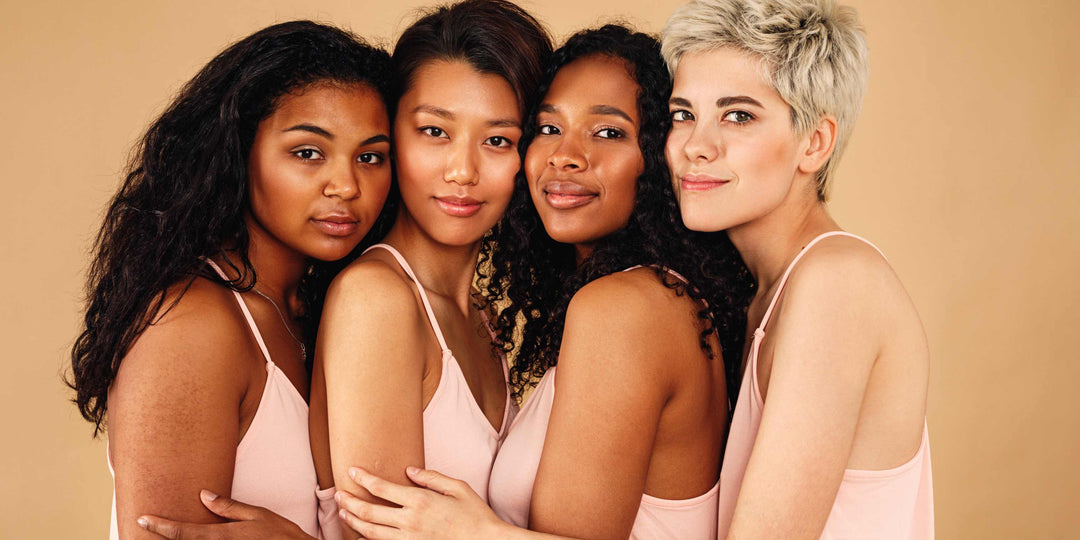 Four women hugging one another from the side glancing toward the camera